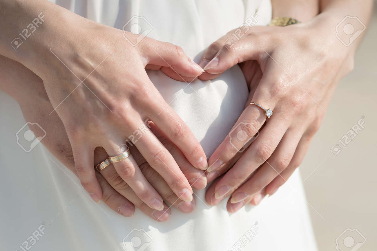 妊娠中の女性の腹に 4 つの手。妊娠中の母親の腹を指で心をポーズの 