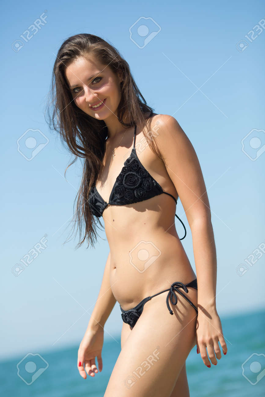 海で女の子 笑みを浮かべてカメラを見て海岸に沿って歩く黒いビキニで魅力的な女の子 の写真素材 画像素材 Image 65398562