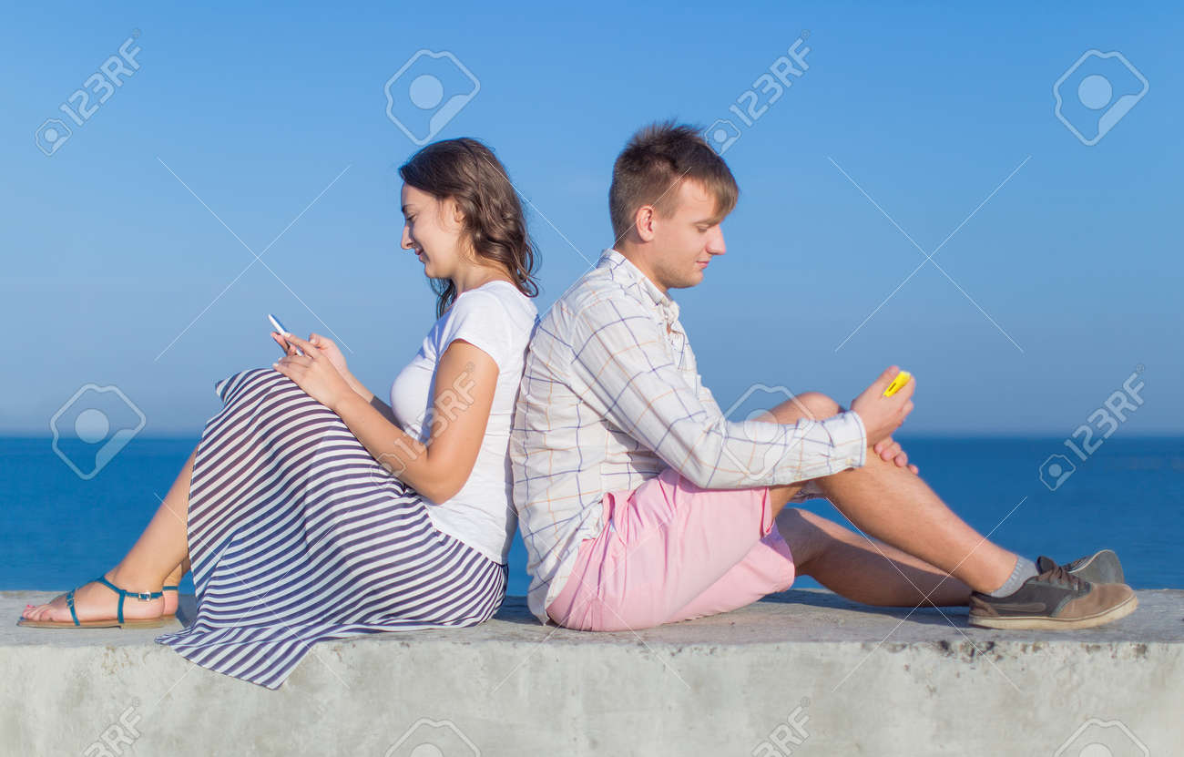 Casal Atraente Em Frente Ao Mar Jovem E Jovem Sentado De Costas Para Tras No Cais De Concreto E Olhando Telas De Smartphones Proprios Fotos Retratos Imagenes Y Fotografia De Archivo Libres