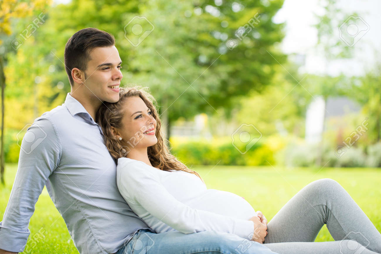 Happy and young pregnant couple in park in summer - 45030077 Happy and young pregnant couple in park in summer - 45030077