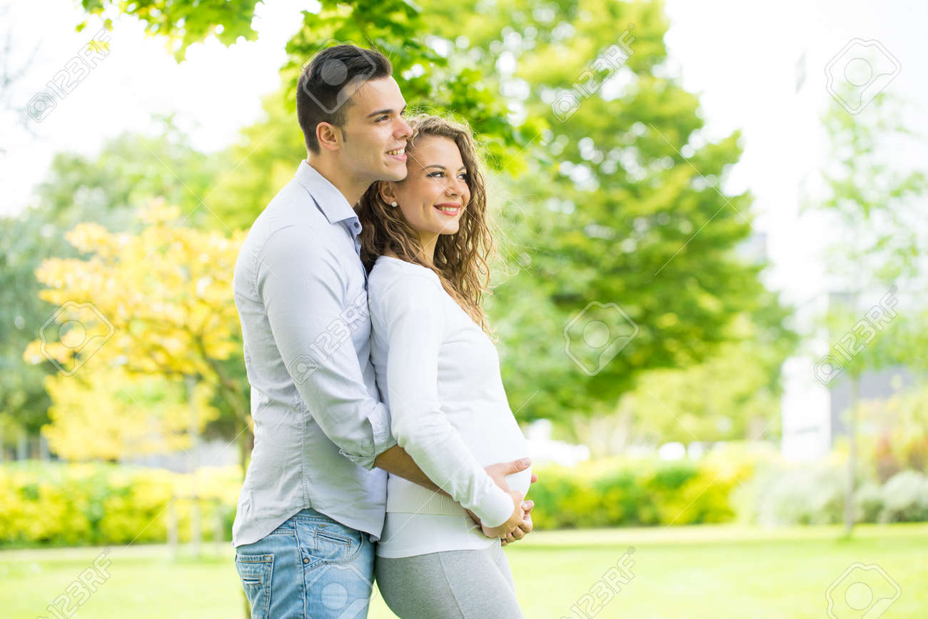 Happy and young pregnant couple in park in summer - 45030111 Happy and young pregnant couple in park in summer - 45030111