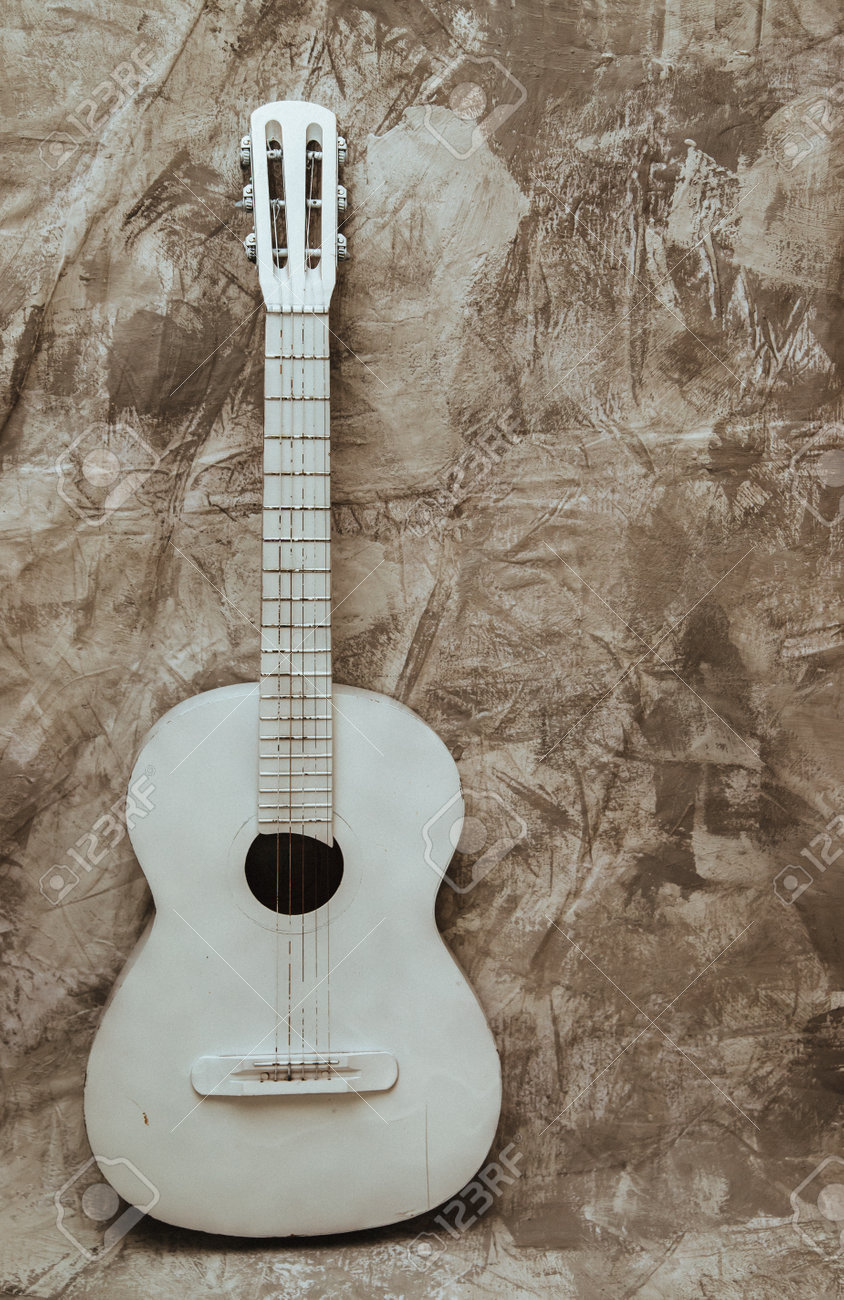 A white old guitar stands against a textured gray wall. Guitar as an object in the interior. Decor and decoration. Broken guitar. - 161360156 A white old guitar stands against a textured gray wall. Guitar as an object in the interior. Decor and decoration. Broken guitar. - 161360156
