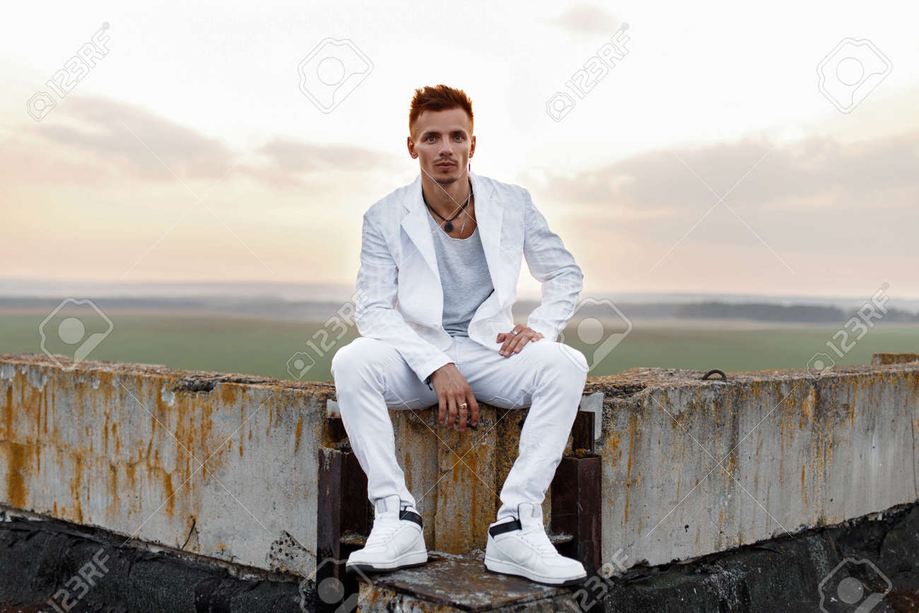 屋根の上に座ってスタイリッシュな白衣の若いハンサムな男 の写真素材 画像素材 Image