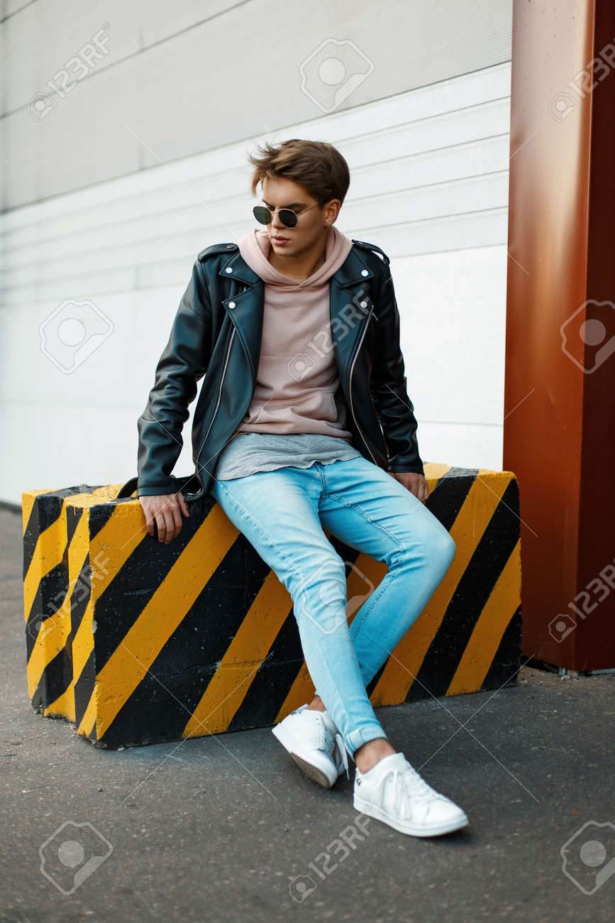 黒と黄色のスラブ上に黒い革のジャケット ブルー ジーンズ 白スニーカーのサングラスでハンサムな若い男が座っています の写真素材 画像素材 Image 0510