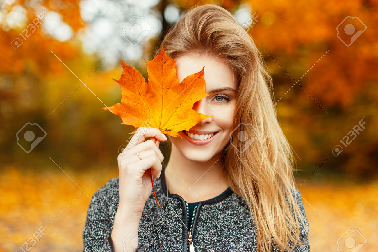 Beautiful happy woman with a smile holds an autumn yellow leaf near the face - 90921795 Beautiful happy woman with a smile holds an autumn yellow leaf near the face - 90921795