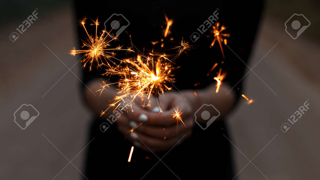 Amazing festive sparklers in the hands of a young woman. Girl celebrates happy birthday. Bright orange sparks with a close up. - 119101696 Amazing festive sparklers in the hands of a young woman. Girl celebrates happy birthday. Bright orange sparks with a close up. - 119101696