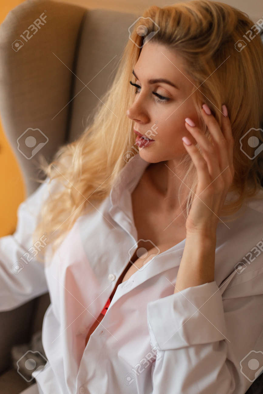 かわいい顔とおっぱい かわいいおっぱいと白いシャツのかわいい顔を持つ美しい若いブロンドの女の子のセクシーな肖像画は、肘掛け椅子に座って休んでいますの写真素材・画像素材  Image 181654961