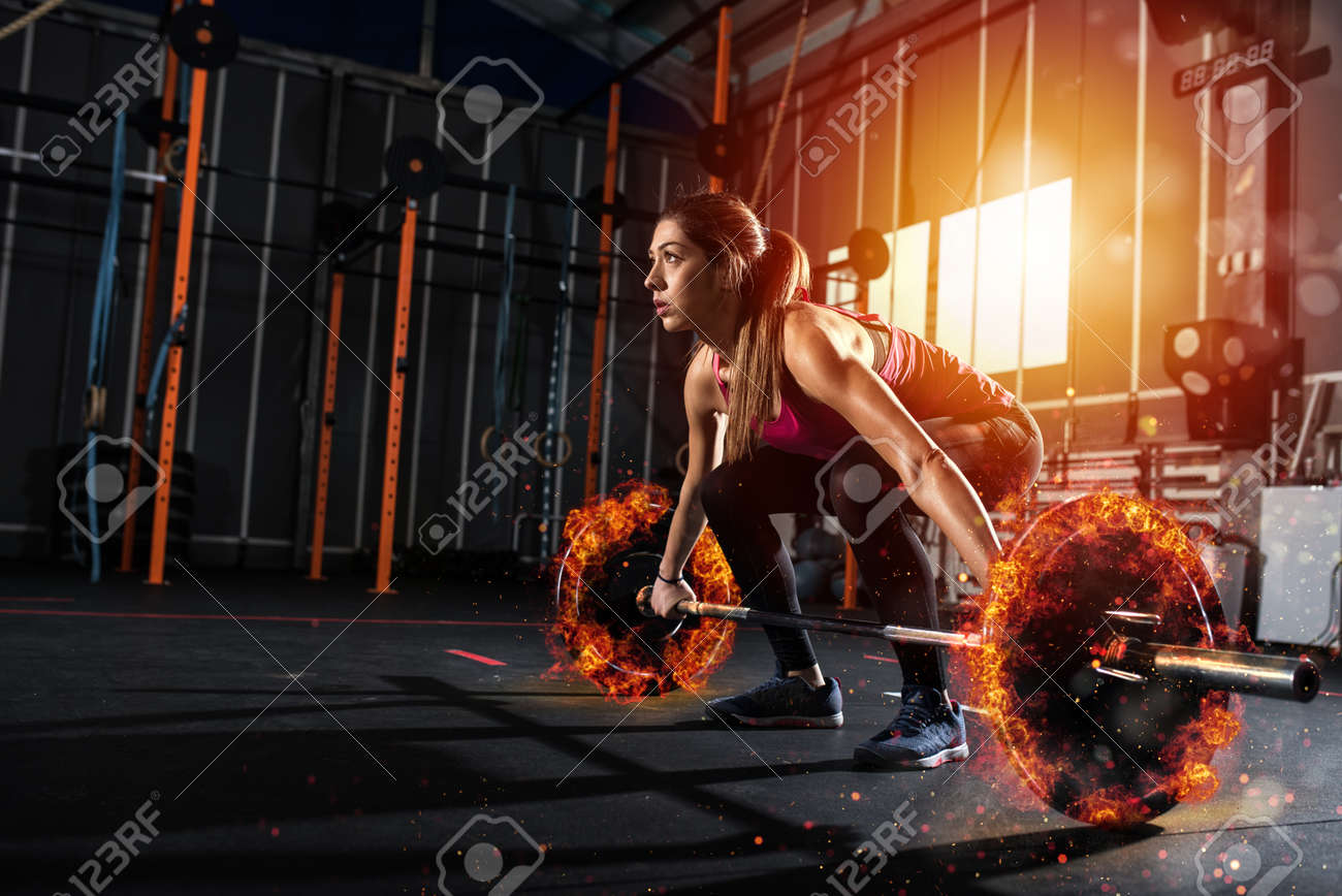 Athletic girl works out at the gym with a fiery barbell - 94766416 Athletic girl works out at the gym with a fiery barbell - 94766416