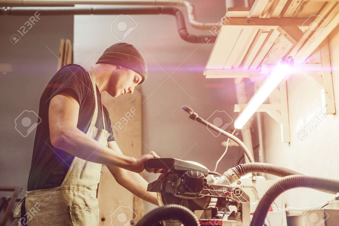 Man in apron using circular saw - 115953570 Man in apron using circular saw - 115953570