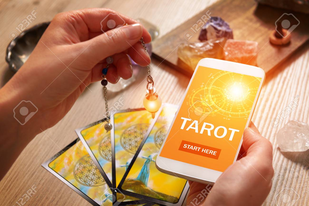 Tarot cards dowsing tool in hand and smartphone with modern fortunetelling application on screen as a concept of psychic advisor or newest ways of divination - 96100547 Tarot cards dowsing tool in hand and smartphone with modern fortunetelling application on screen as a concept of psychic advisor or newest ways of divination - 96100547