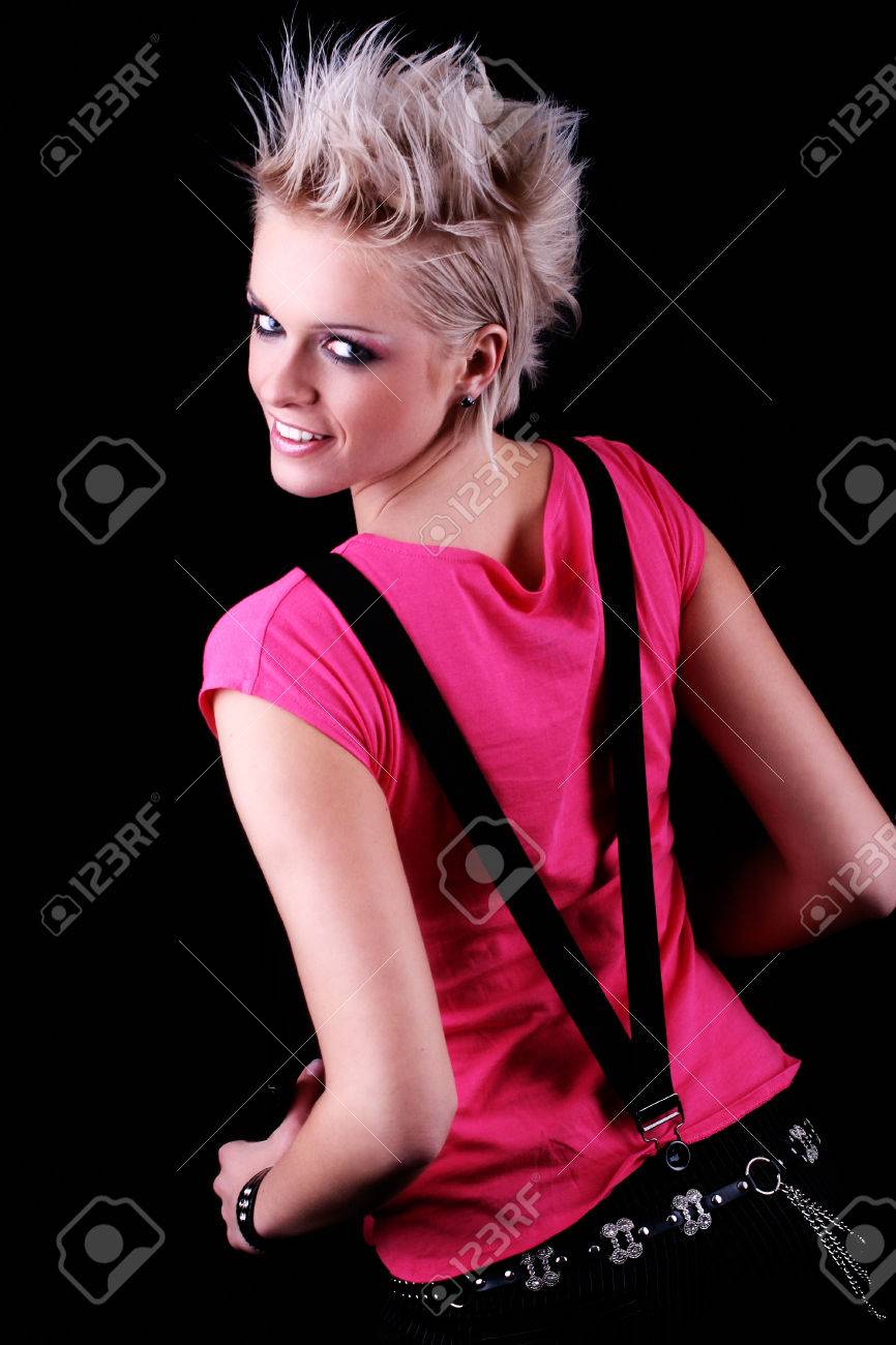 高角ピンクのトップと彼女の肩越しに振り返ってみると暗いスタジオに対して笑顔で中かっこを着てファンキーなとがった金髪の髪型でかわいいモダンな若い女性の肖像 の写真素材 画像素材 Image