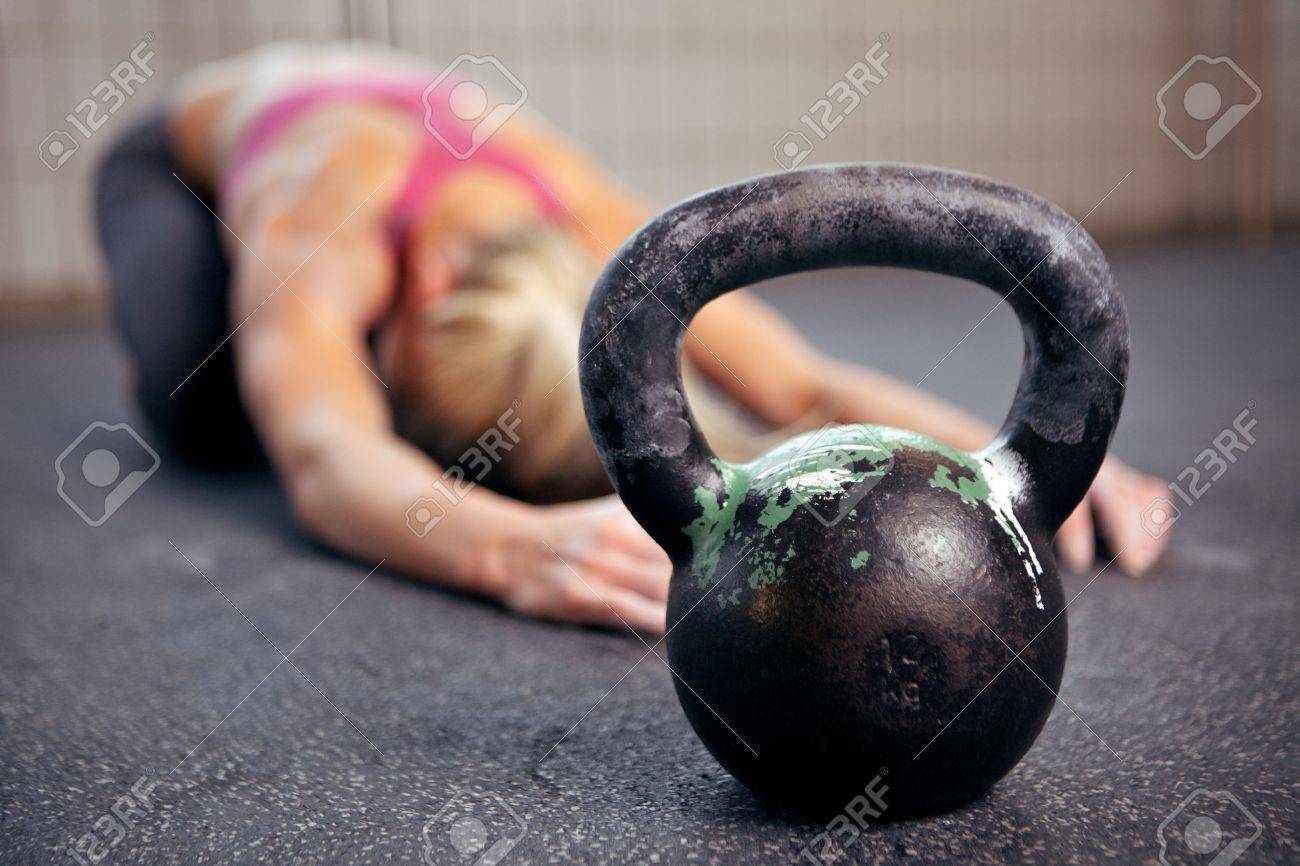 Young woman stretching her back after a heavy kettlebell workout in a gym - 14158006 Young woman stretching her back after a heavy kettlebell workout in a gym - 14158006