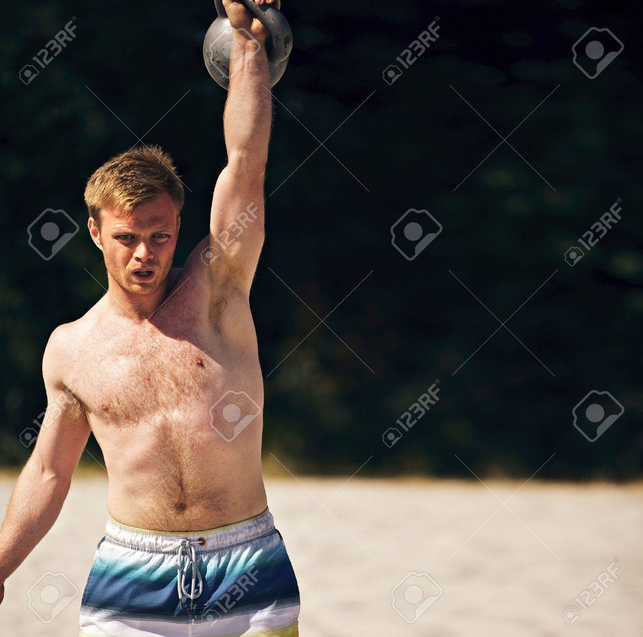 guy lifting a heavy kettlebell on a beach during crossfit workout