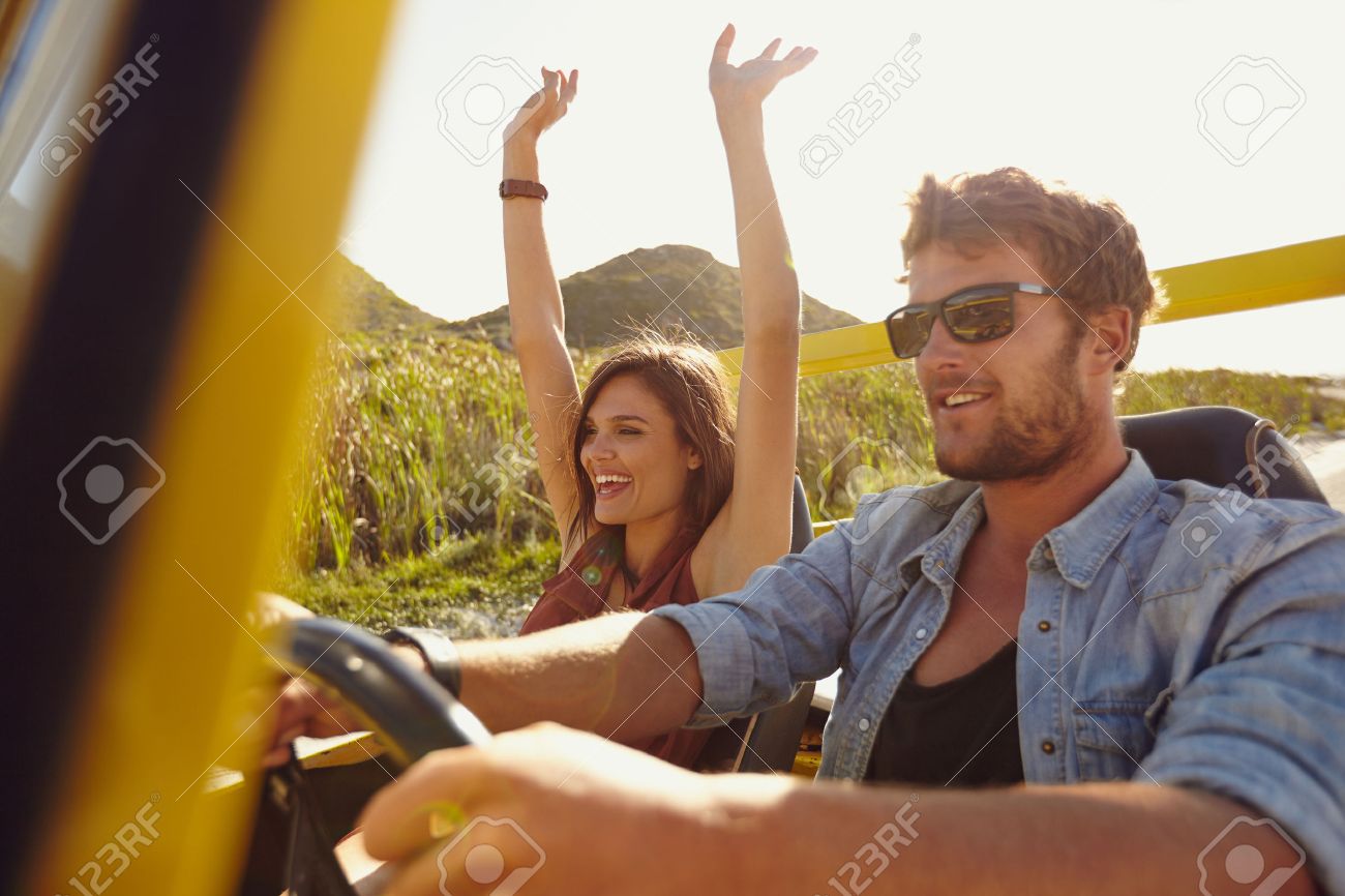 久しぶりに楽しんで幸せなカップルは 車でドライブします 道路に行く友人は夏の日旅行します 白人の若い男は彼女の腕を上げるとうれしそうな女性 車を運転します の写真素材 画像素材 Image