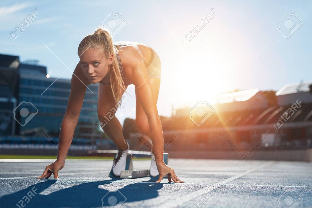 Professional female track athlete in set position on sprinting blocks of an athletics running track. Runner is in a athletics stadium with bright sunlight. - 46875016 Professional female track athlete in set position on sprinting blocks of an athletics running track. Runner is in a athletics stadium with bright sunlight. - 46875016