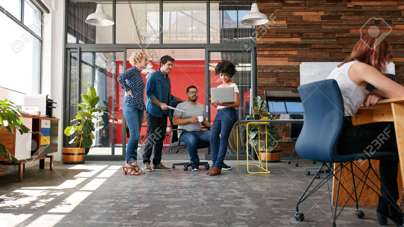 Portrait of group of creative people having a meeting with a laptop in a modern office. Business people having relaxed conversation over new project. - 51510750 Portrait of group of creative people having a meeting with a laptop in a modern office. Business people having relaxed conversation over new project. - 51510750