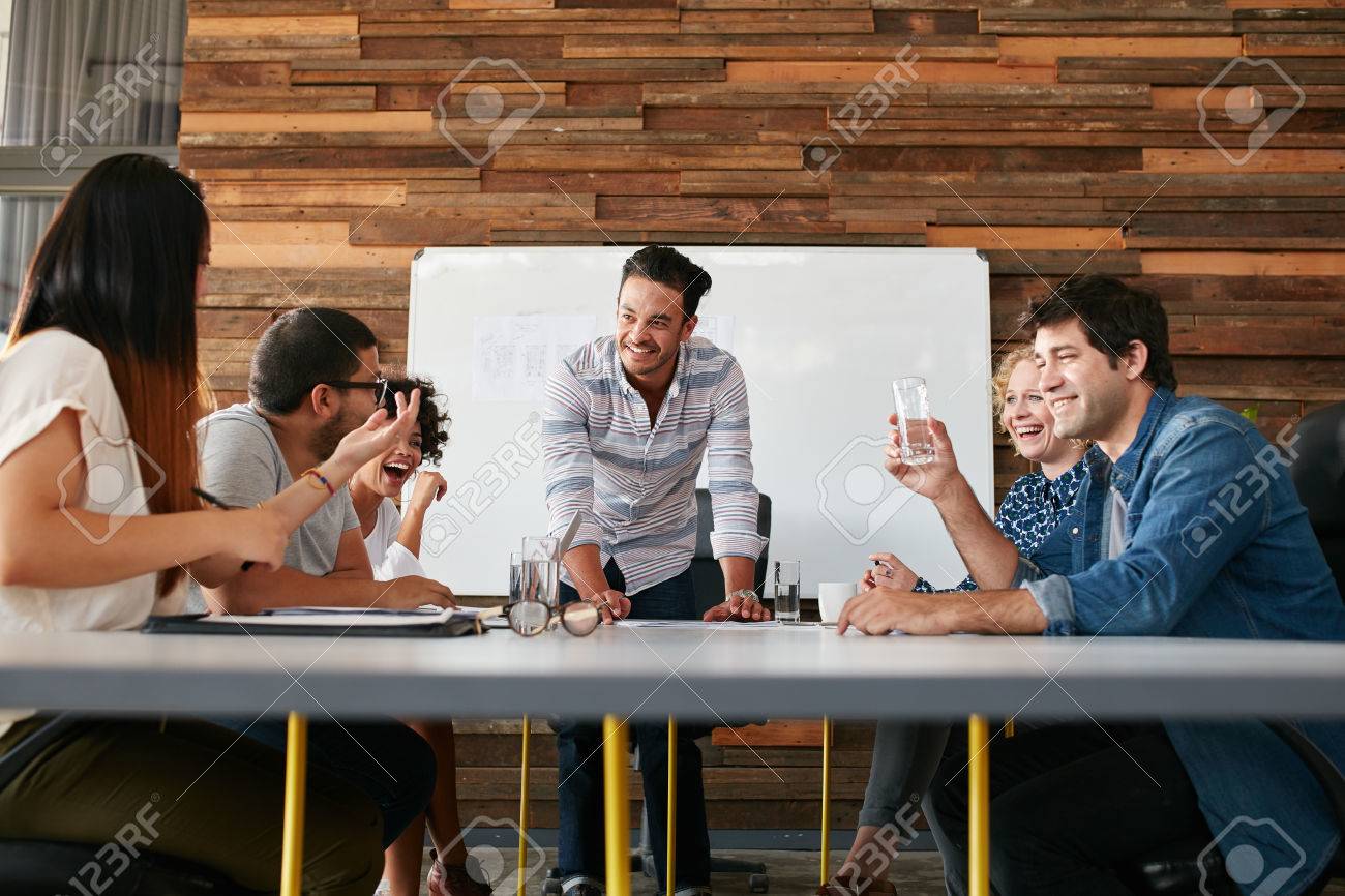Group of happy young people having a business meeting. Creative people sitting at table in boardroom with man explaining business strategy. - 51510795 Group of happy young people having a business meeting. Creative people sitting at table in boardroom with man explaining business strategy. - 51510795
