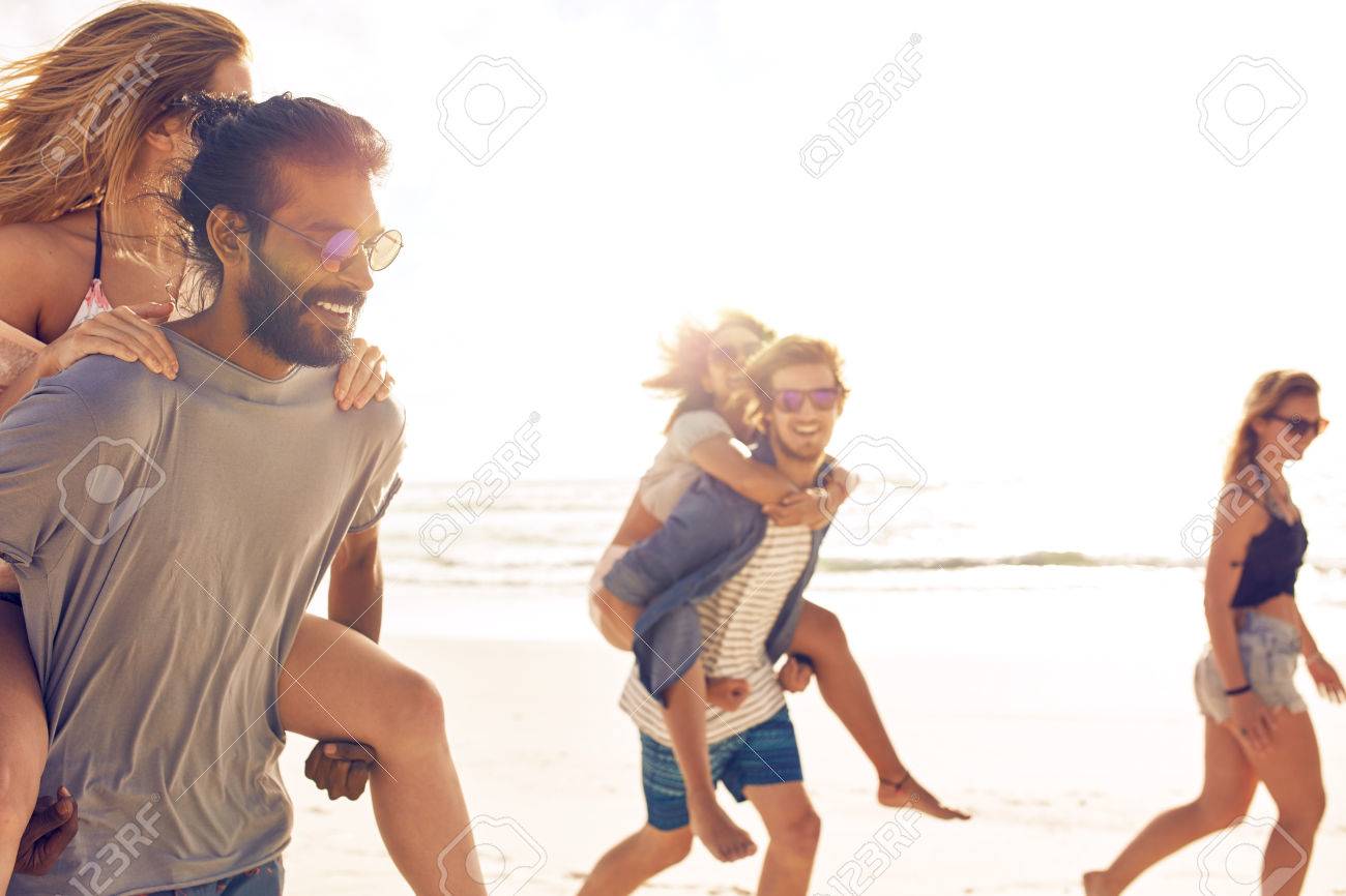 海の海岸に女性をピギーバックの若い男性 ビーチ上で楽しんで友人のグループ 混血の若い人が夏休みを楽しんでいます の写真素材 画像素材 Image