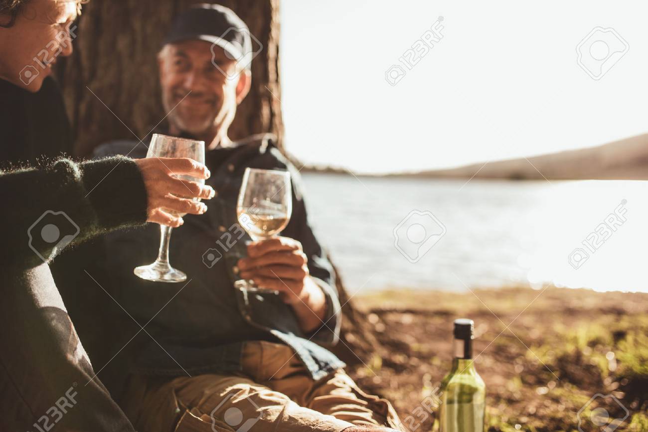 湖の近くでキャンプしながらワインを飲む年配のカップルの肖像画を閉じます 両手のワインに焦点を当てます の写真素材 画像素材 Image