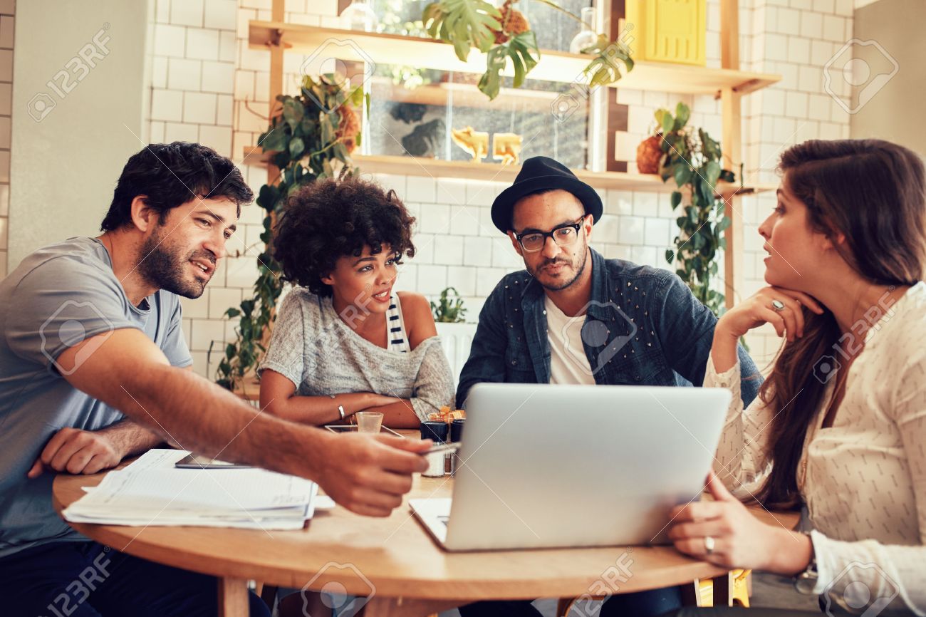 portrait of young people sitting around a table in cafe with stock