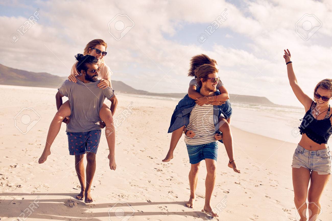 男性女性におんぶを与えるとビーチで楽しんで若いお友達の多様なグループは 幸せな若い人々 がビーチで夏休みを楽しんでいます の写真素材 画像素材 Image