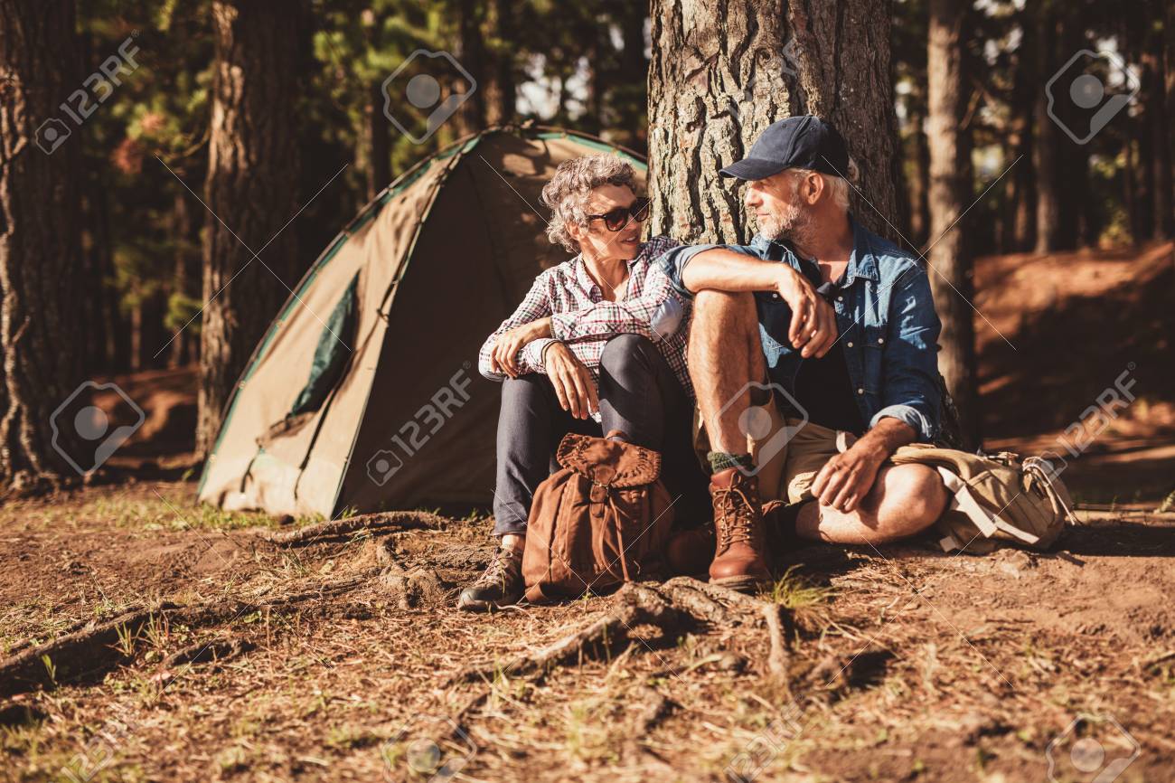夏の日に一緒にツリーの下に座って幸せな先輩カップルの肖像画 成熟した男と女付近のテントの中 森でのキャンプします の写真素材 画像素材 Image