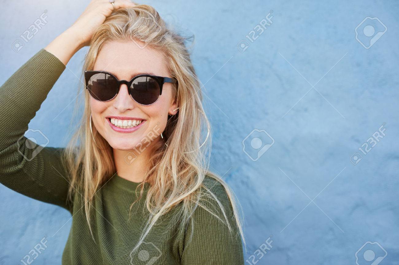 Close up shot of pretty young woman in sunglasses smiling. Attractive young female model with copy space on blue background. - 62293945 Close up shot of pretty young woman in sunglasses smiling. Attractive young female model with copy space on blue background. - 62293945