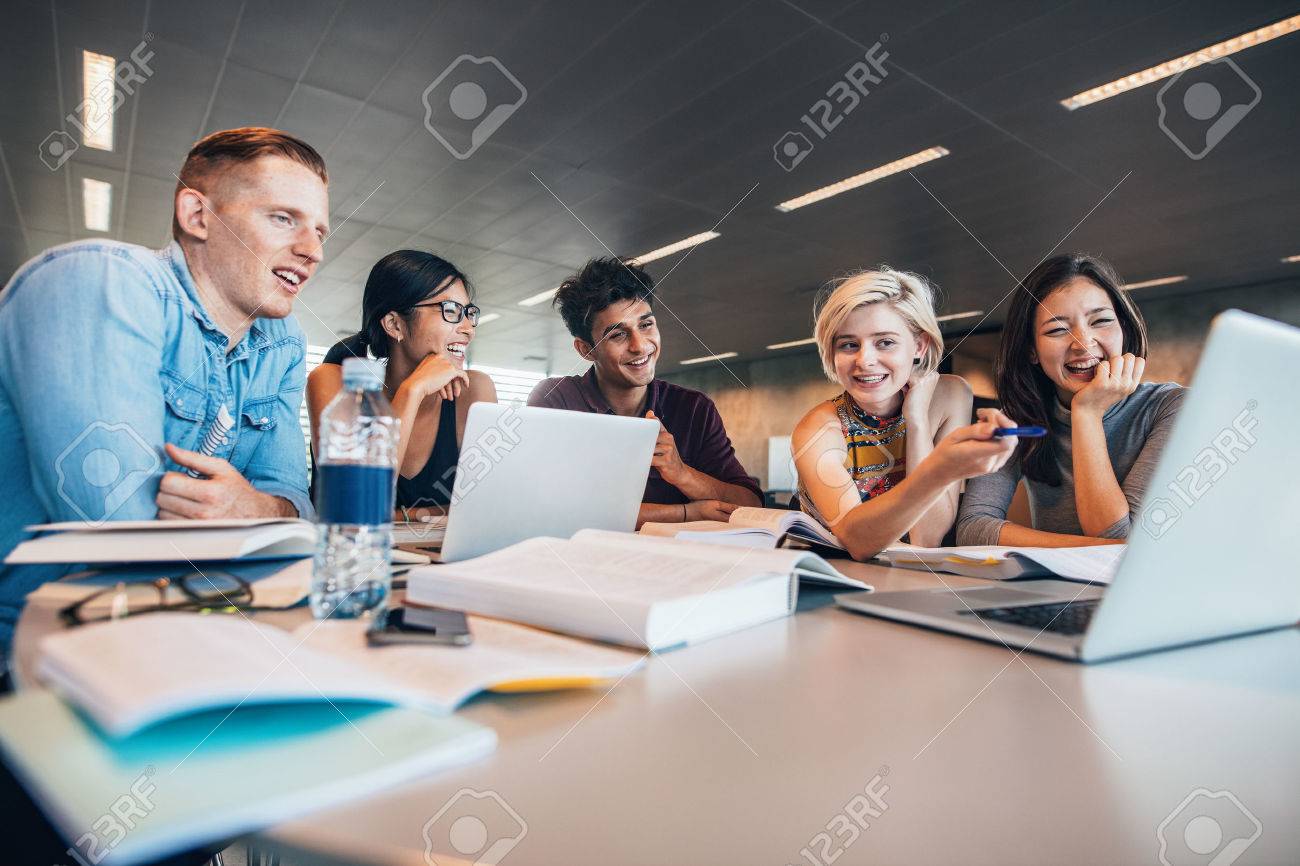 University students sitting together at table with books and looking at laptop. Happy young people doing group study in library. - 70199366 University students sitting together at table with books and looking at laptop. Happy young people doing group study in library. - 70199366