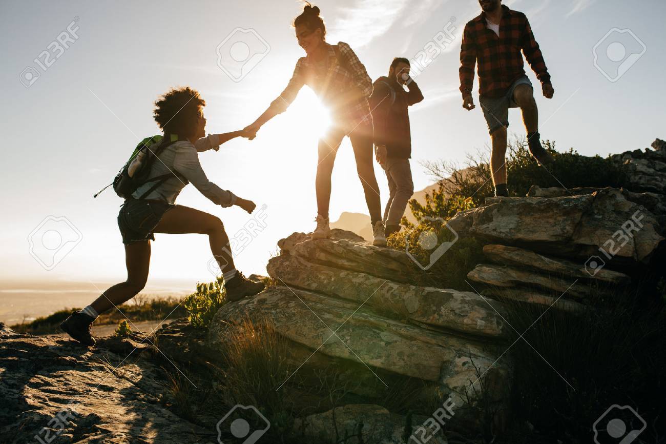 Group of hikers on a mountain. Woman helping her friend to climb a rock. Young people on mountain hike at sunset. - 71836814 Group of hikers on a mountain. Woman helping her friend to climb a rock. Young people on mountain hike at sunset. - 71836814