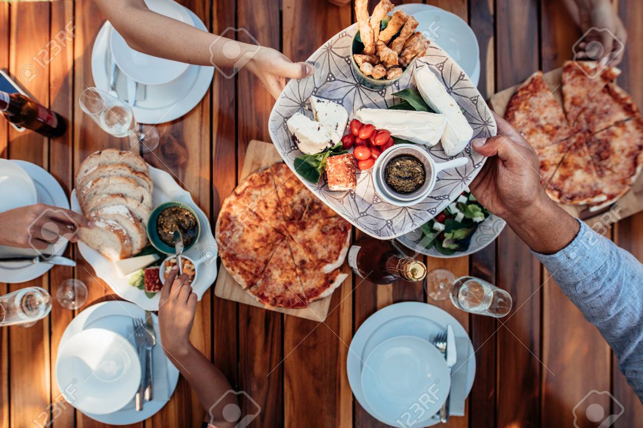 テーブルで食事を食べている人々 の平面図は パーティーのため提供しています 新築祝いを祝うパーティーは木製のテーブルの上 男性の手が女性のゲストにお皿を渡します の写真素材 画像素材 Image