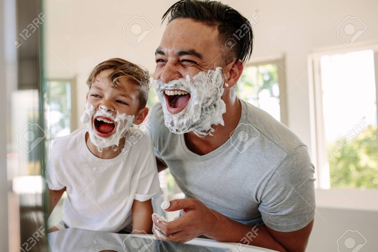 Man and little boy with shaving foam on their faces looking into the bathroom mirror and laughing. Father and son having fun while shaving in bathroom. - 92941156 Man and little boy with shaving foam on their faces looking into the bathroom mirror and laughing. Father and son having fun while shaving in bathroom. - 92941156