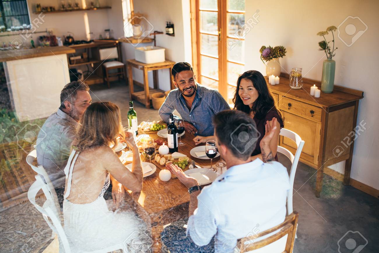 ディナーパーティー中にテーブルに座って話している友人たち 一緒に食べ物を食べ 家でパーティーを楽しむために集まる人々 の写真素材 画像素材 Image