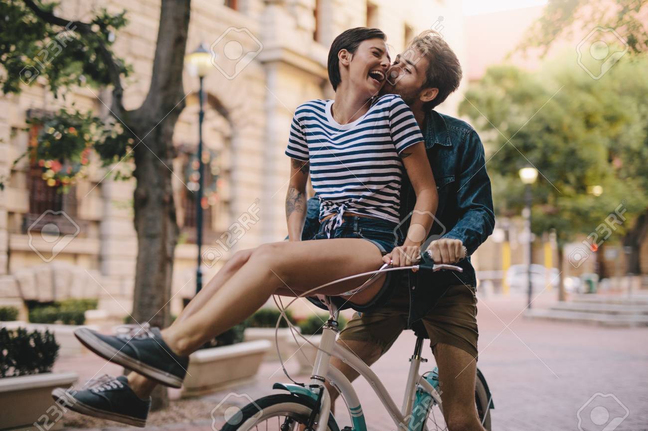 100844361-laughing-woman-sitting-on-boyfriends-bicycle-handlebar-cheerful-couple-on-a-bike-together-in-the-cit.jpg
