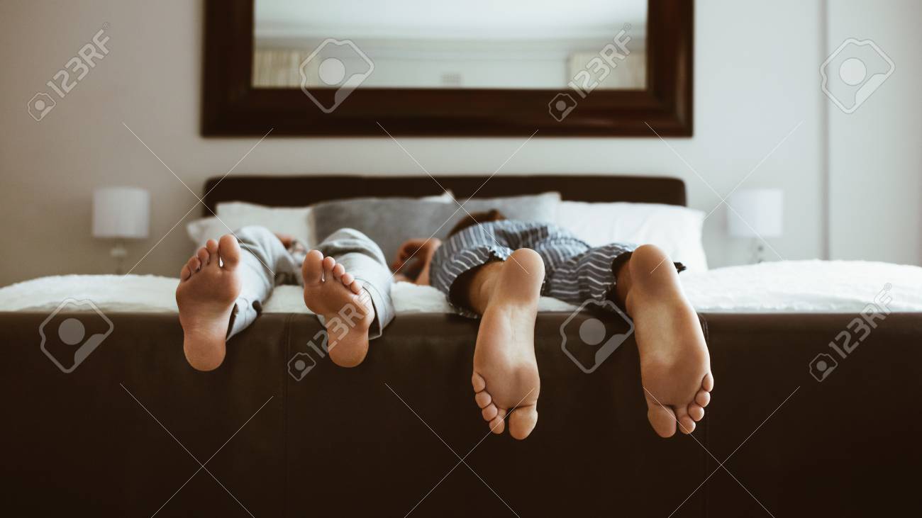 Feet of two people sleeping on bed. People sleeping on bed in different positions. - 107260253 Feet of two people sleeping on bed. People sleeping on bed in different positions. - 107260253
