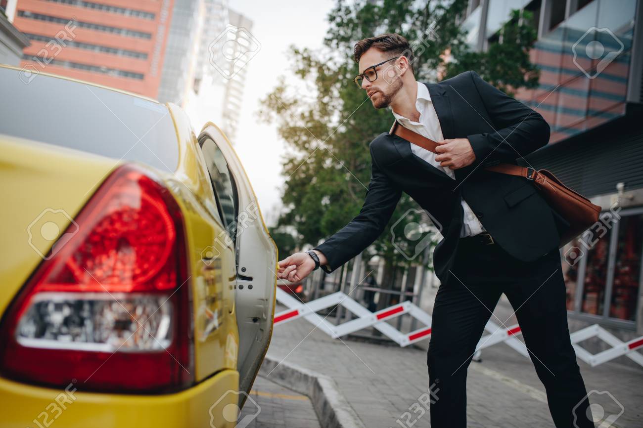 Entrepreneur opening the door of a taxi standing on the pavement. Man taking a taxi to go to office. - 112007432 Entrepreneur opening the door of a taxi standing on the pavement. Man taking a taxi to go to office. - 112007432