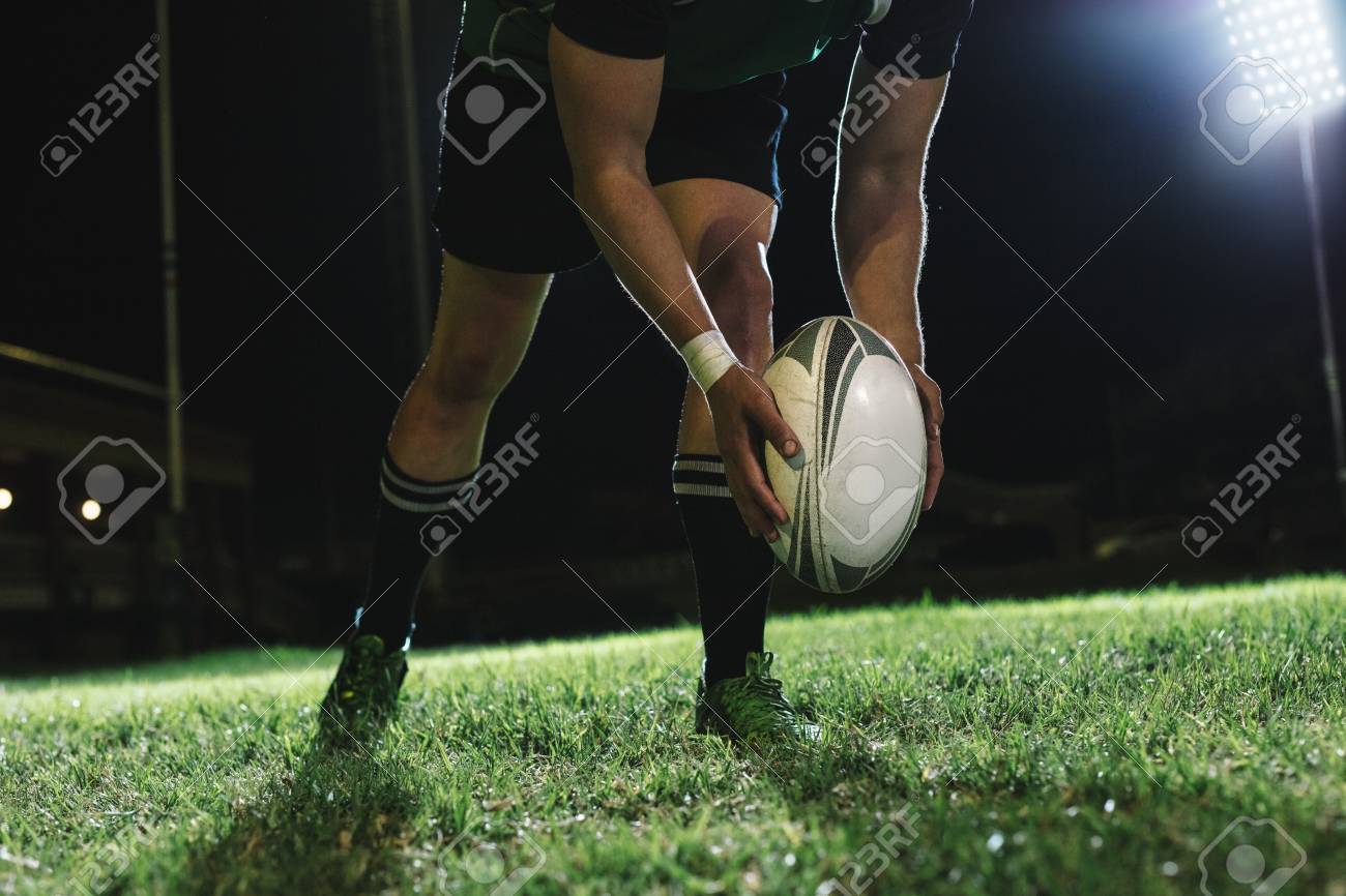 Rugby player dropping the ball to the ground for kicking as it touches the ground. - 116932442 Rugby player dropping the ball to the ground for kicking as it touches the ground. - 116932442