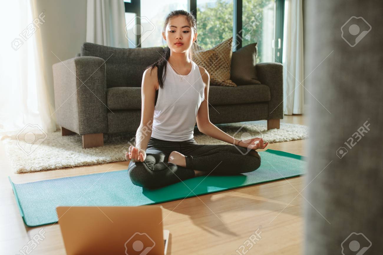 Fit woman doing yoga exercise while watching tutorial on laptop at home. Attractive chinese woman exercising on a mat and watching instructional videos on laptop. - 118799630 Fit woman doing yoga exercise while watching tutorial on laptop at home. Attractive chinese woman exercising on a mat and watching instructional videos on laptop. - 118799630