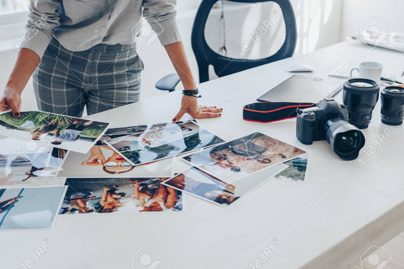 Woman standing at her desk and choosing the best images from photoshoot. Female photographer looking at the photo prints on table. - 120521227 Woman standing at her desk and choosing the best images from photoshoot. Female photographer looking at the photo prints on table. - 120521227