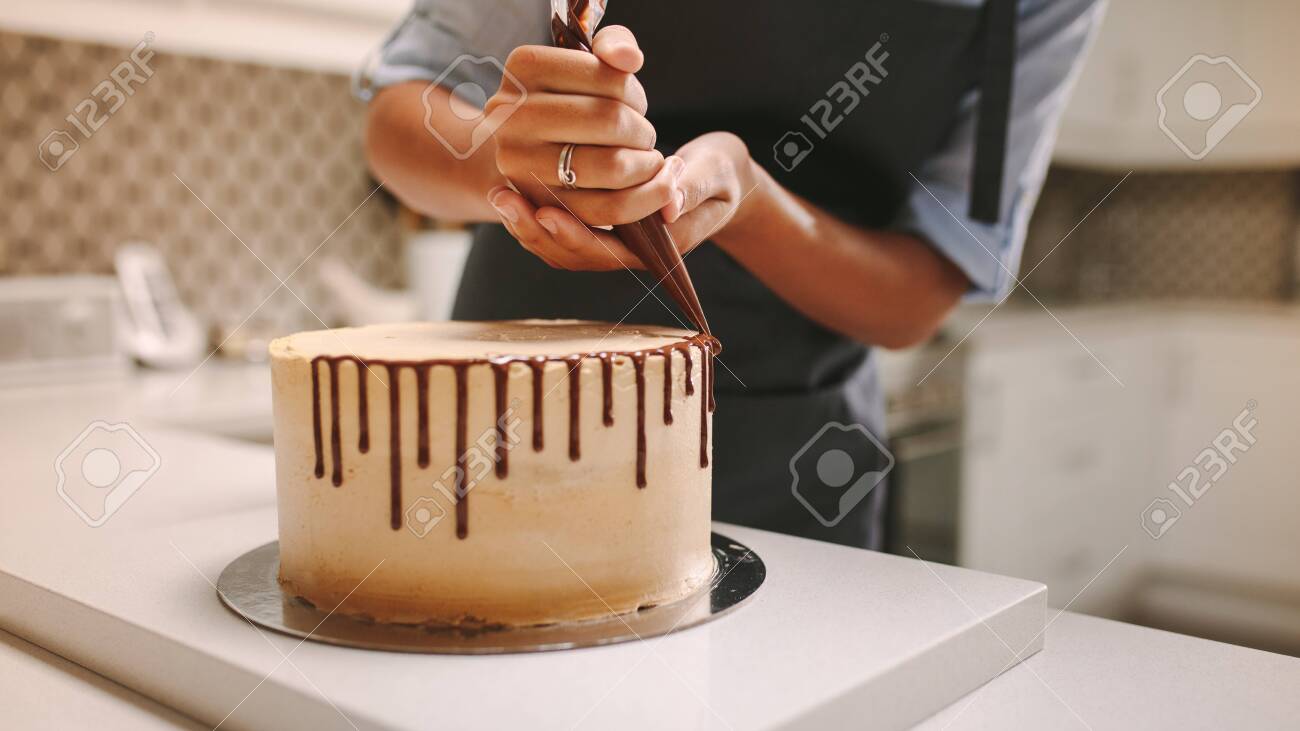 Close up of hands of a female chef with confectionery bag squeezing liquid chocolate on cake. - 124105087 Close up of hands of a female chef with confectionery bag squeezing liquid chocolate on cake. - 124105087