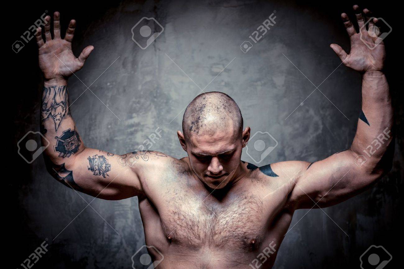 muscular tattooed man with hands raised up posing over grey