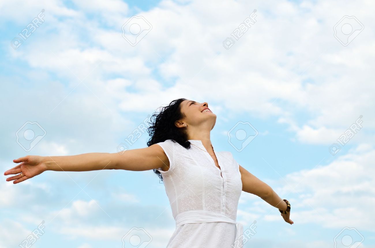 Happy smiling woman standing with outspread arms and her face lifted to the cloudy blue sky - 14615066 Happy smiling woman standing with outspread arms and her face lifted to the cloudy blue sky - 14615066