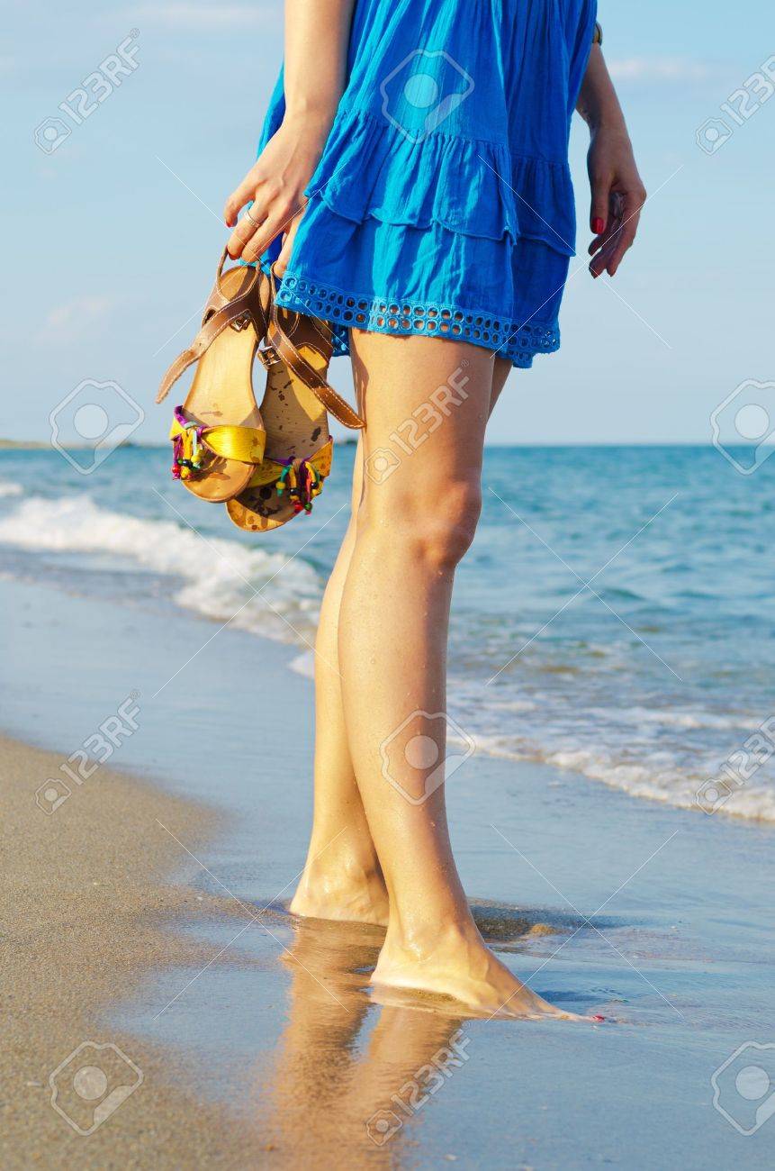 Woman holding her sandals in her hands while standing in wet sand at the edge of the surf on a beach - 14889376 Woman holding her sandals in her hands while standing in wet sand at the edge of the surf on a beach - 14889376