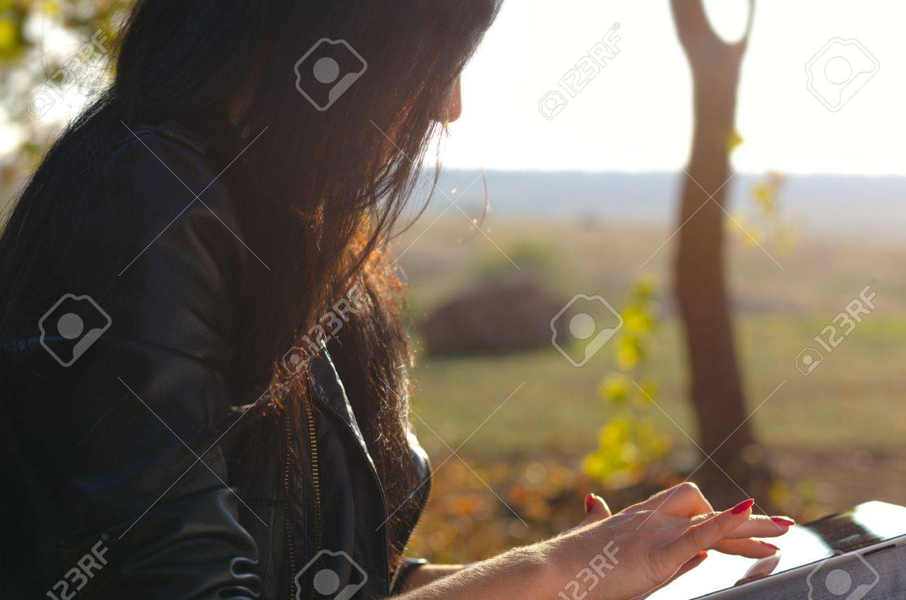 Closeup cropped side view of a woman using a tablet touching the screen with her finger against a background of open countryside - 16638066 Closeup cropped side view of a woman using a tablet touching the screen with her finger against a background of open countryside - 16638066