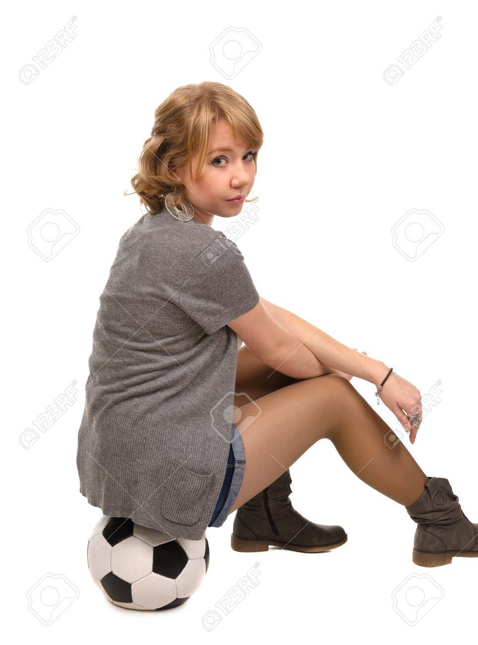 カメラは 白で隔離のスタジオ ポートレートを彼女の肩越しに振り返ってサッカー ボールの上に座ってパンツでかなりブロンドの女の子 の写真素材 画像素材 Image