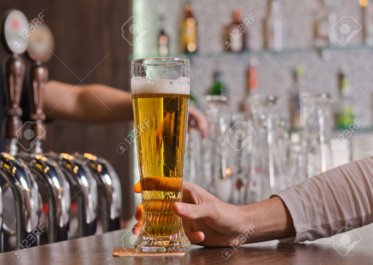 Man sitting at a counter in the bar holding a full pint glass of beer, close up view of his hand with the taps for dispensing draught beer alongside - 23833411 Man sitting at a counter in the bar holding a full pint glass of beer, close up view of his hand with the taps for dispensing draught beer alongside - 23833411