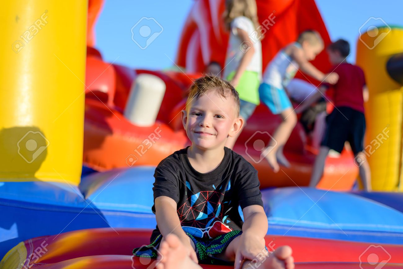 Smiling happy barefoot little boy sitting on a colorful inflatable plastic jumping castle at a fairground or kids playground - 41912277 Smiling happy barefoot little boy sitting on a colorful inflatable plastic jumping castle at a fairground or kids playground - 41912277