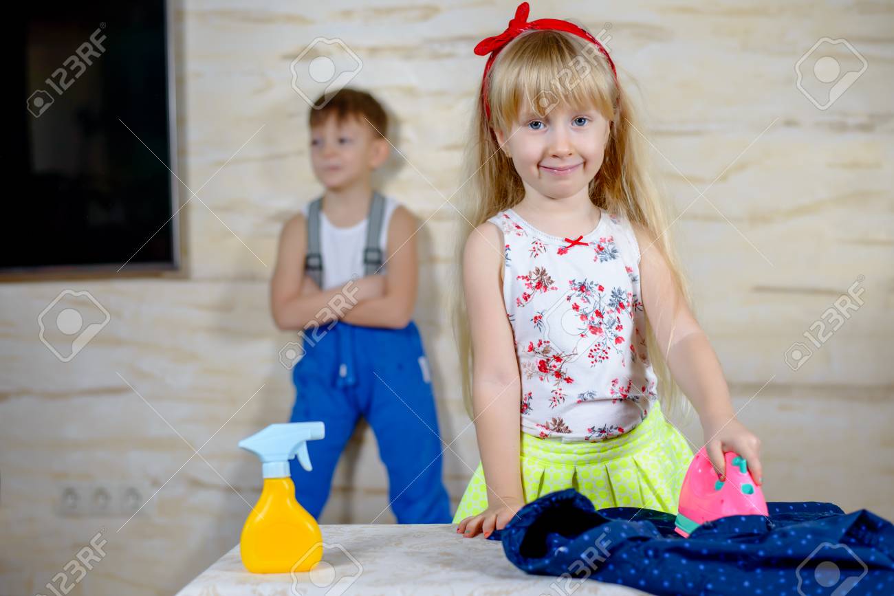 Frohlich Kleines Blondes Madchen Das Bugeln Zu Tun Einen Plastik Rosa Spielzeug Eisen Mit Grinst Glucklich Wie Sie In Die Kamera Kleiner Junge Im Hintergrund Sieht Lizenzfreie Fotos Bilder Und Stock Fotografie