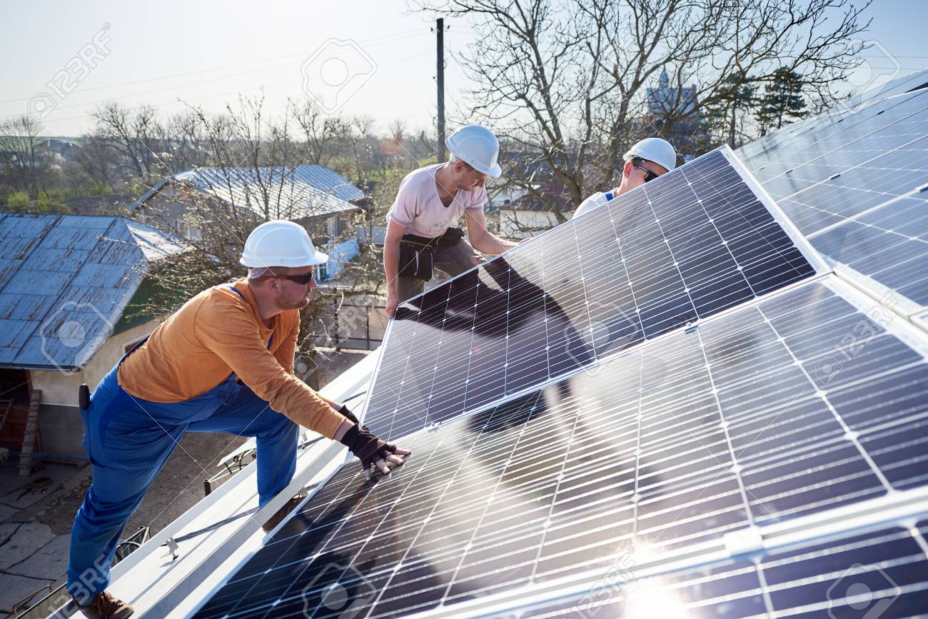Male workers installing solar photovoltaic panel system. Electricians mounting blue solar module on roof of modern house. Alternative energy ecological concept. - 120141569 Male workers installing solar photovoltaic panel system. Electricians mounting blue solar module on roof of modern house. Alternative energy ecological concept. - 120141569