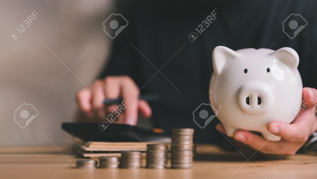 돼지 저금통과 사람과 함께 동전을 쌓으면 월별 가계 예산을 관리하거나 지출 부기 개념을 계획하여 수입과 지출을 계산합니다. 로열티 무료  사진, 그림, 이미지 그리고 스톡포토그래피. Image 173909828