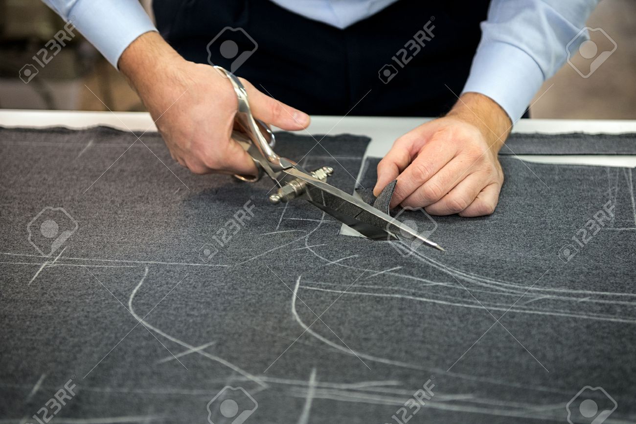 tailor cutting fabric using large scissors or shears as he follows